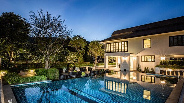 Um hotel moderno com uma grande piscina ao ar livre, rodeado por vegetação exuberante e áreas de estar ao ar livre bem iluminadas.