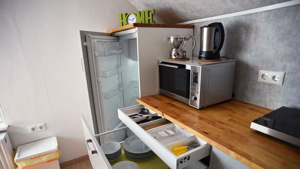 Une cuisine compacte équipée d’un four à micro-ondes, d’un grille-pain et d’une machine à café sur le plan de travail. On y trouve également un petit réfrigérateur et un tiroir contenant de la vaisselle.