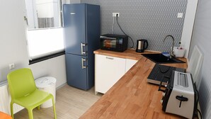 Une cuisine de taille réduite, avec un réfrigérateur bleu, un grille-pain, une bouilloire et un évier.