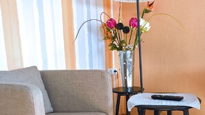 Un salon moderne avec un canapé, une petite table sur laquelle se trouve une télécommande, une lampe et un vase rempli de fleurs.