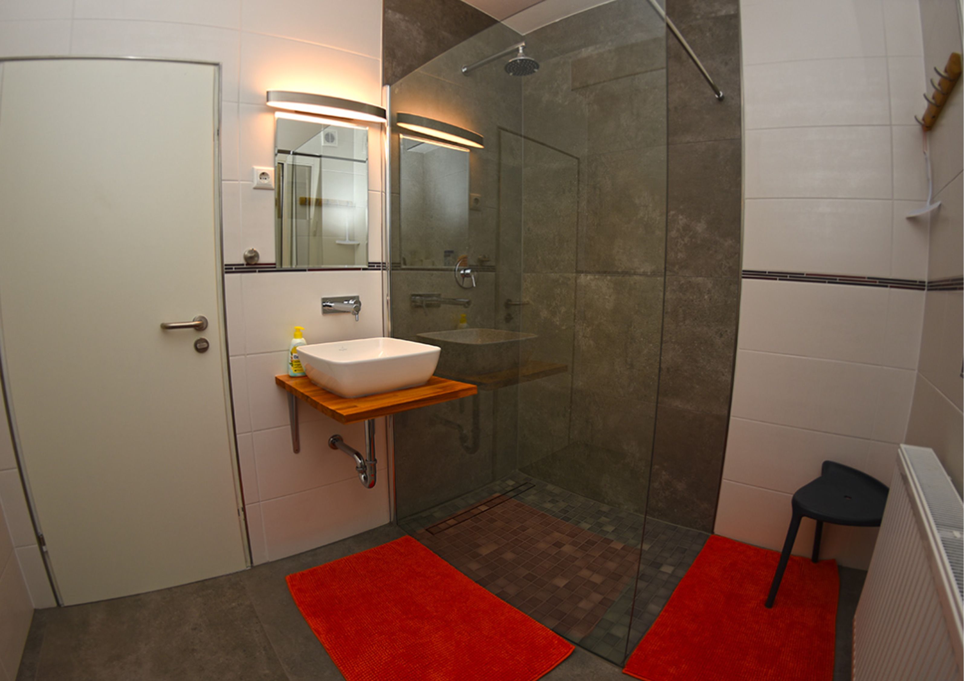 Ein Badezimmer mit einem weißen Waschbecken, einer Duschkabine aus Glas und einem roten Teppich.