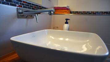Eine weiße, freistehende Badewanne mit Chromarmatur, einer gefliesten Rückwand und Holzboden.