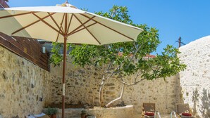 A poolside area with lounge chairs, a sun umbrella, and a stone wall. - Dotira, an Enchanting Heritage Home with Pool (Rethimno)