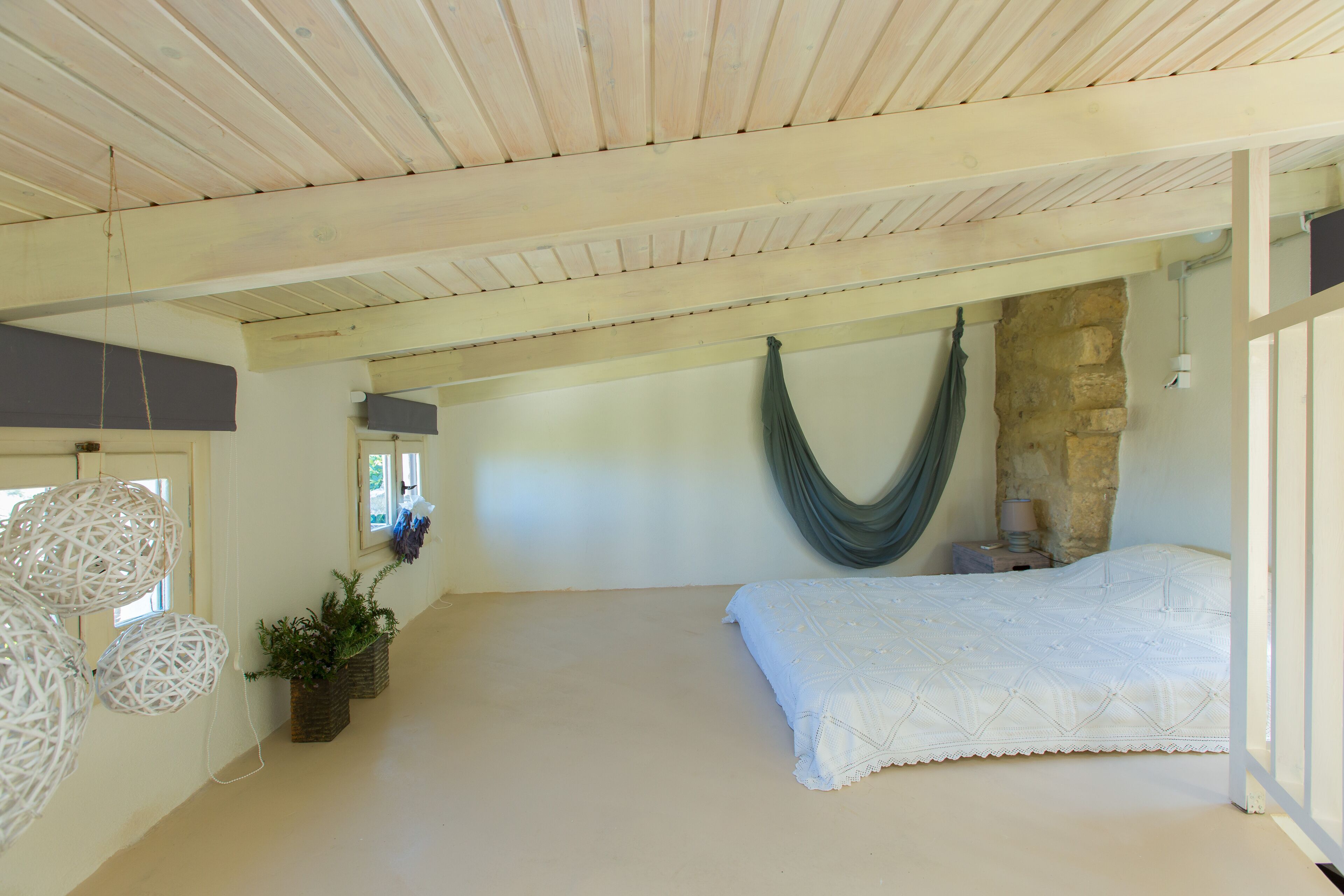 A bedroom with a hammock, a bed, and a stone wall.