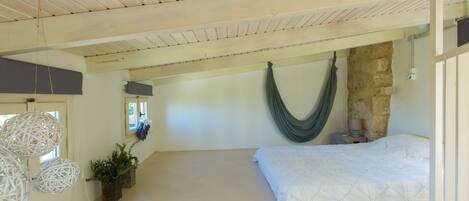 A bedroom with a hammock, a bed, and a stone wall.