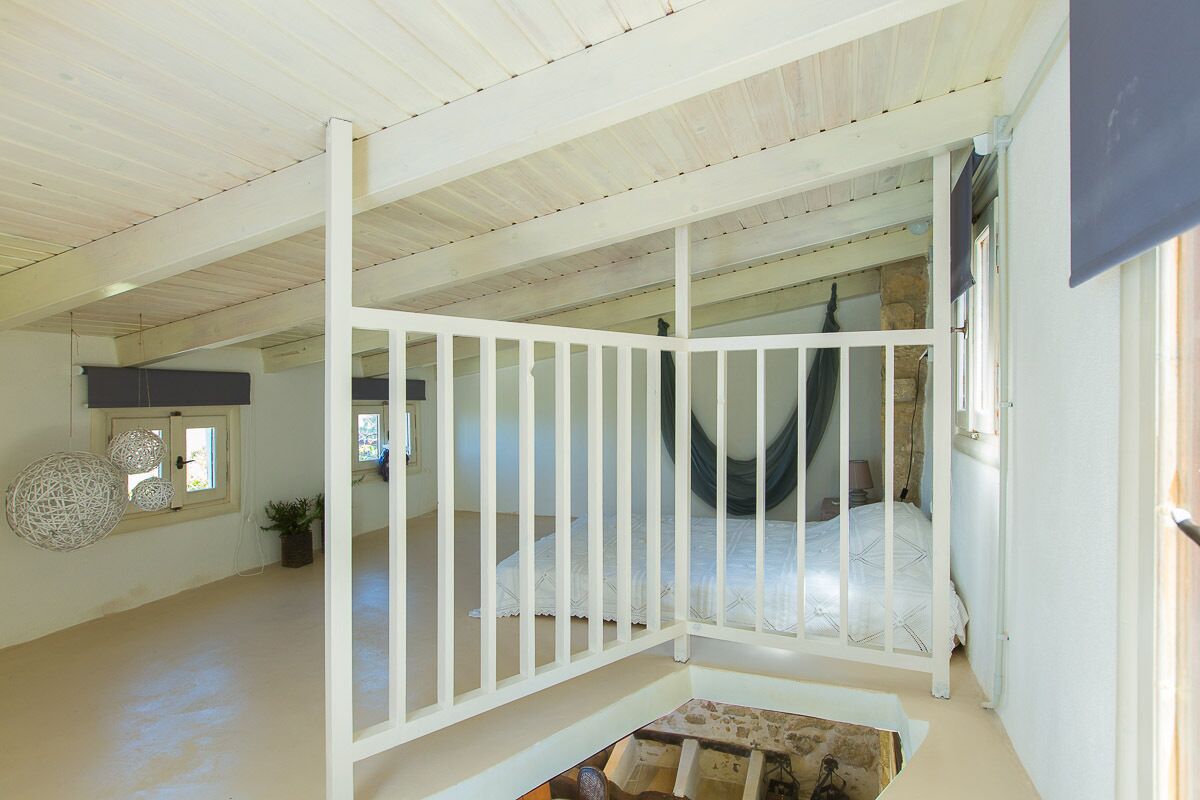 A spacious room with a high ceiling, a white bed, and a view of a stone wall.