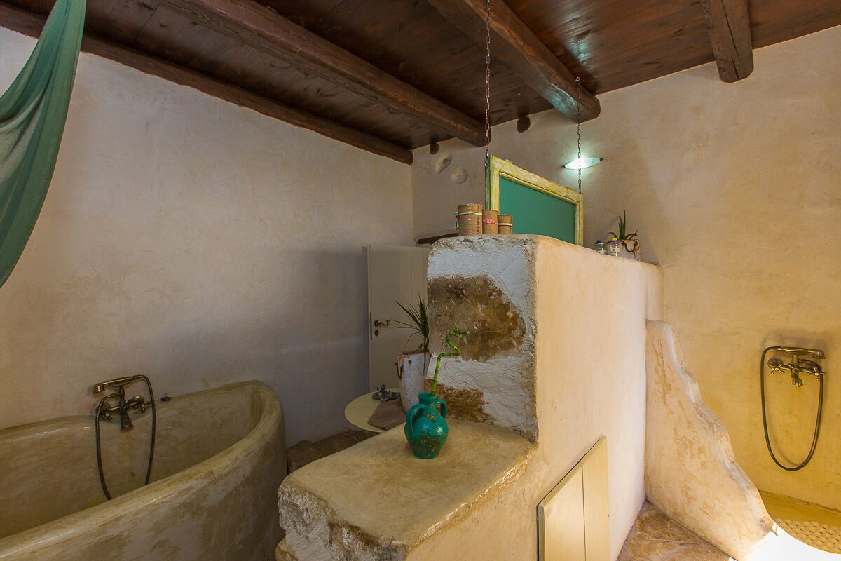 A rustic bathroom with a bathtub, a shower, and a small sink area with a vase and plants.