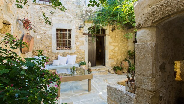 A stone courtyard with a bed, potted plants, and a bench. - Dotira, an Enchanting Heritage Home with Pool (Rethimno)