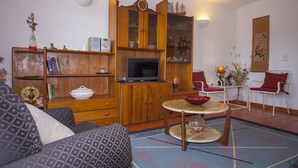 A living room with a wooden cabinet, a television, a dining table with chairs, and a red sofa. - D10 - Ferragudo Townhouse by DreamAlgarve (Lagoa)
