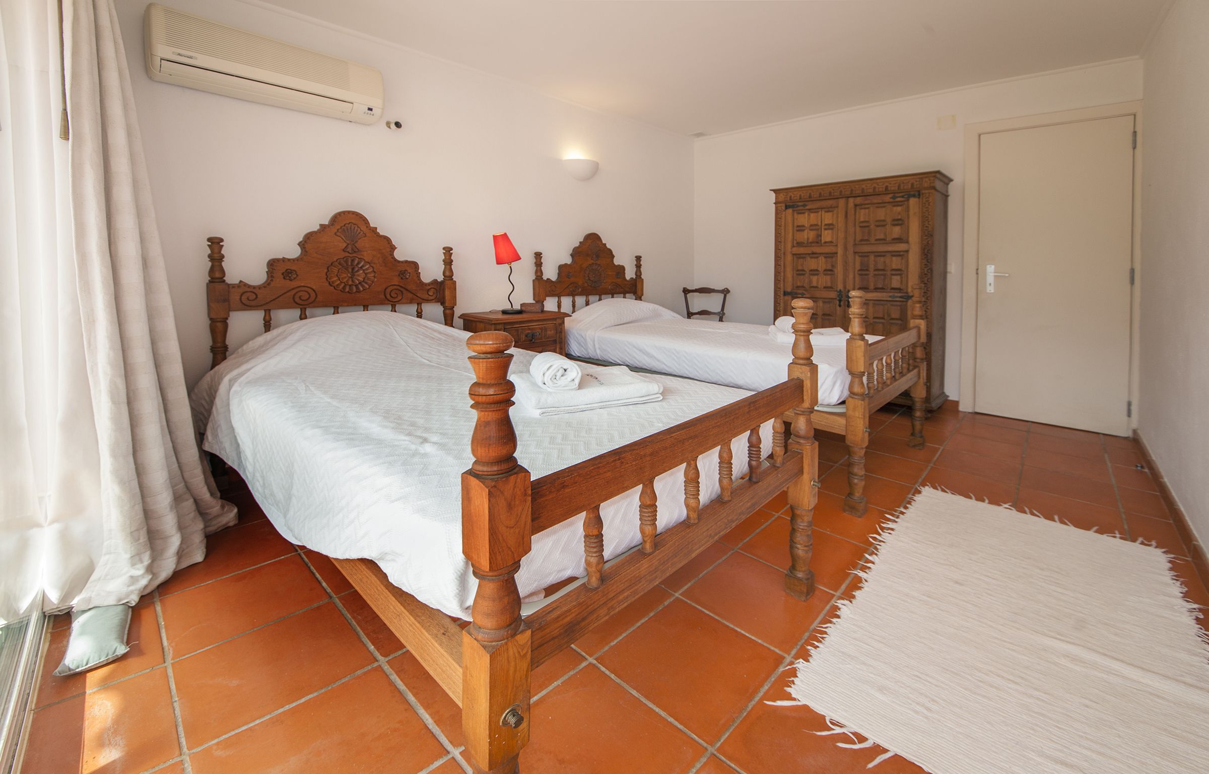 Une chambre à coucher avec deux lits en bois, une table de chevet, une armoire et un tapis blanc.