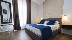 A modern hotel room with a large bed, a mirror, a flat-screen TV, and a brick-patterned wall. - Loft Rooms Trastevere (Rome)