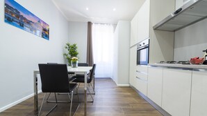 A modern kitchen with white cabinets, a stainless steel range hood, and a dining area with a table and chairs. - Loft Rooms Trastevere (Rome)