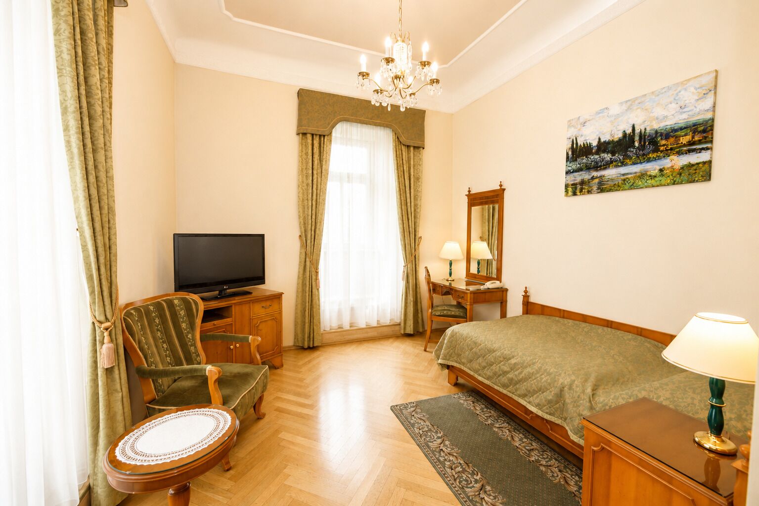 Habitación de hotel con televisión, escritorio con lámpara, cama, sillón y un cuadro en la pared.