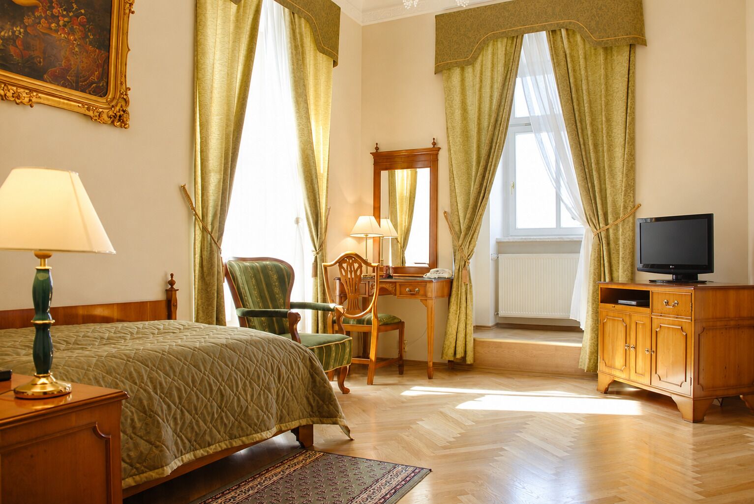 Quarto de hotel com cama, escrivaninha, cadeira, televisão e cortinas.