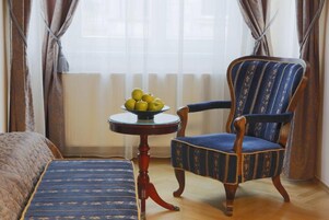 Una habitación con una cama, una silla, una mesita con manzanas y un ventanal con cortinas.