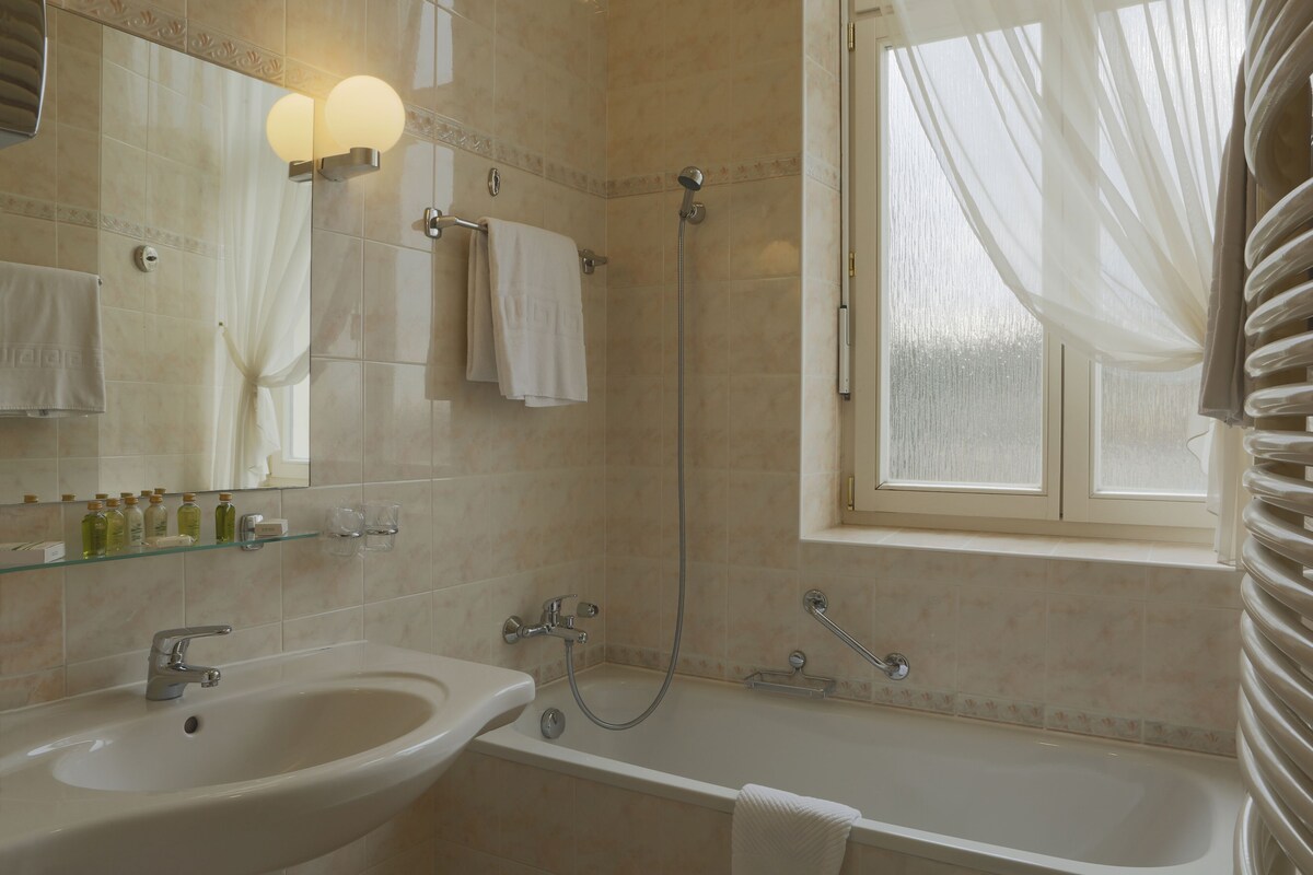Un baño con lavamanos, bañera y ducha. Hay toallas colgadas en la pared y una ventana con cortinas.
