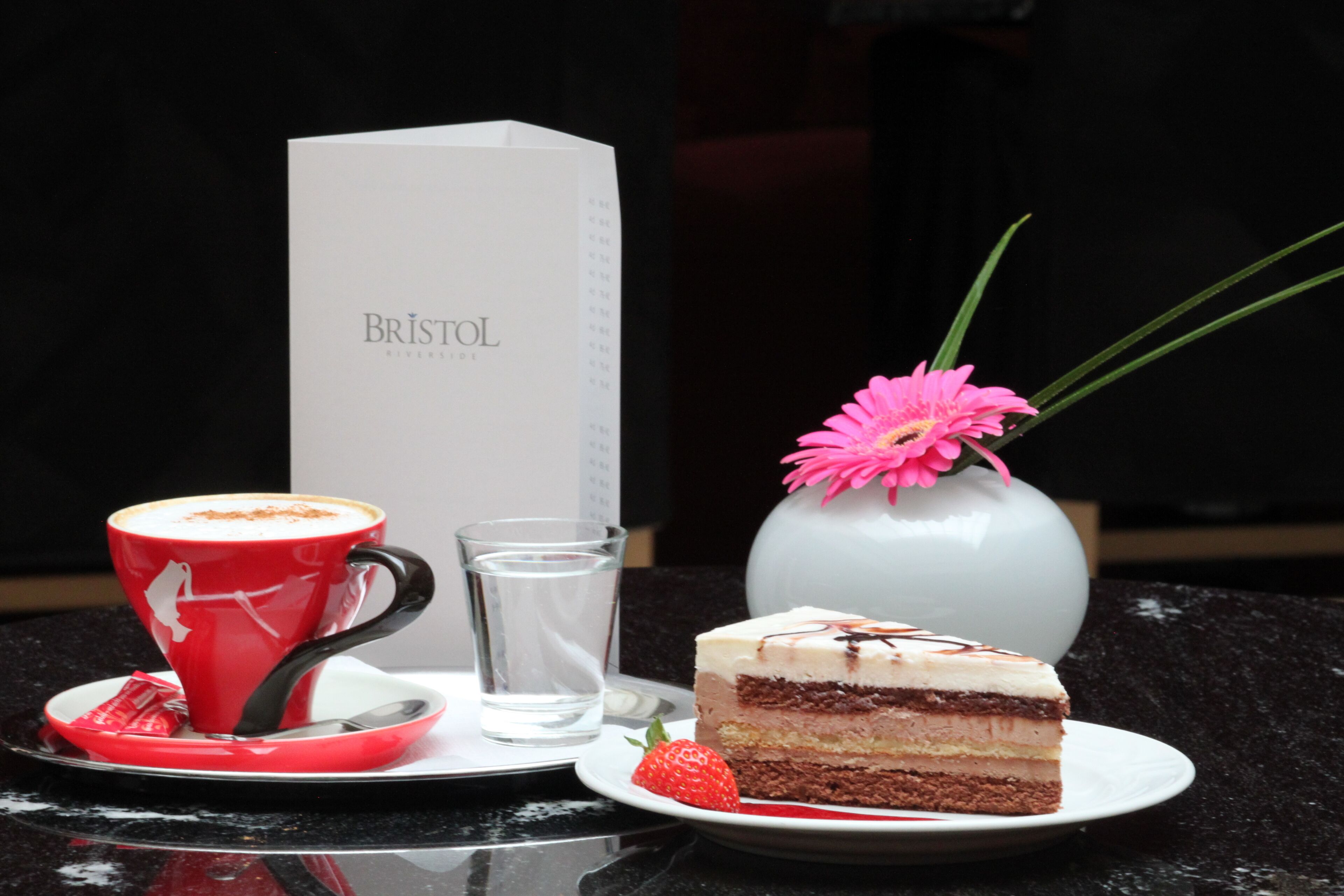 Een dessertopstelling met taart, een kop koffie en een glas water op een tafel.