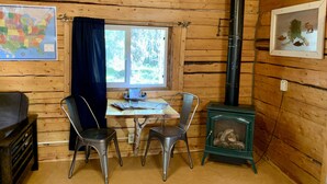 En mysig stuga med träpanel på väggarna, ett bord med stolar, en karta på väggen och en vedkamin.