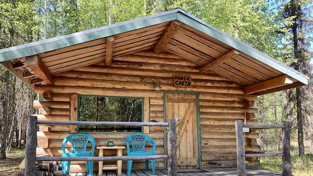 En stuga av trä med en veranda, två blå stolar, ett bord och en skylt med texten ”Älgstugan”.