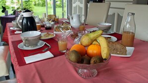 Une table de petit-déjeuner dressée avec une variété de fruits, de pain et de boissons, et offrant une vue sur la verdure environnante.