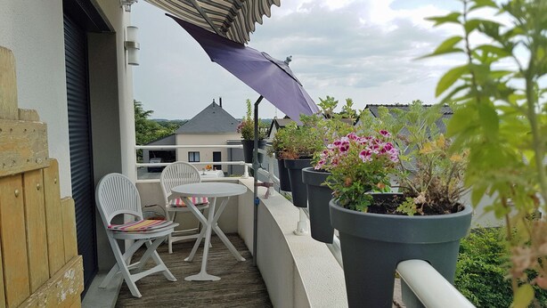 Un balcon doté d’un plancher en bois, de chaises blanches, d’une petite table ronde et de plantes en pot.