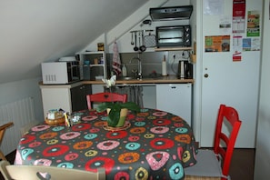 Una cocina compacta con microondas, tostadora y refrigerador. En primer plano, una mesa de comedor con mantel de colores.