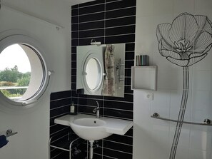 A bathroom with a round window, a white sink, a mirror, and a shower. - Chambres d'hôtes Les 3 Vallées (Mauges-sur-Loire)