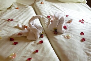 Una cama bien arreglada con dos toallas formando cisnes, decorada con pétalos de rosa y pequeños adornos.