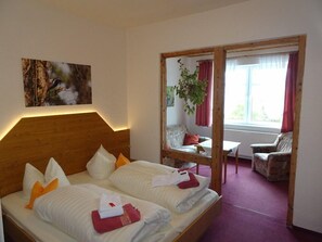 Ett hotellrum med en sänggavel i trä, två sängar med vita sängkläder, en tavla på väggen, ett fönster med gardiner och utsikt över omgivningen.