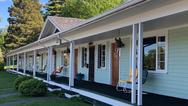 A row of single-story houses with a porch, each with a door and windows, and a small garden area in front. - Edenbrook Motel (Bar Harbor)