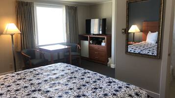A hotel room with a large bed, a desk with a chair, a television, a dresser, and a mirror on the wall.