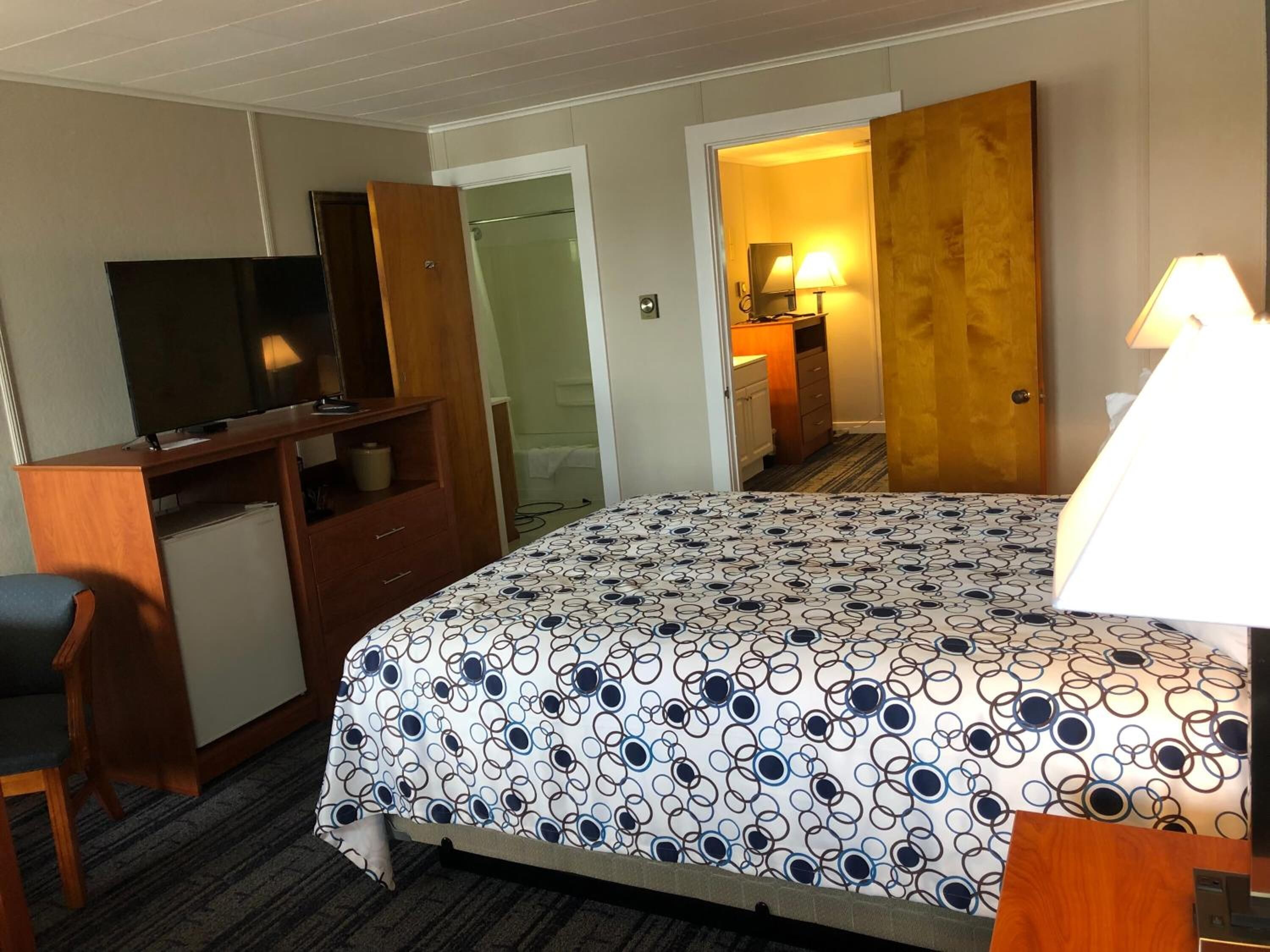 A hotel room with a bed, a desk, a television, and a bathroom visible through an open door.
