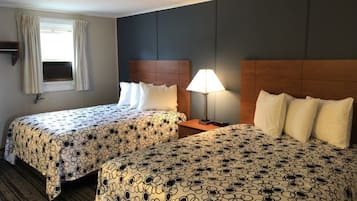 Una habitación de hotel con dos camas, una mesita de noche, una lámpara, una ventana con cortinas y un estante fijado a la pared.