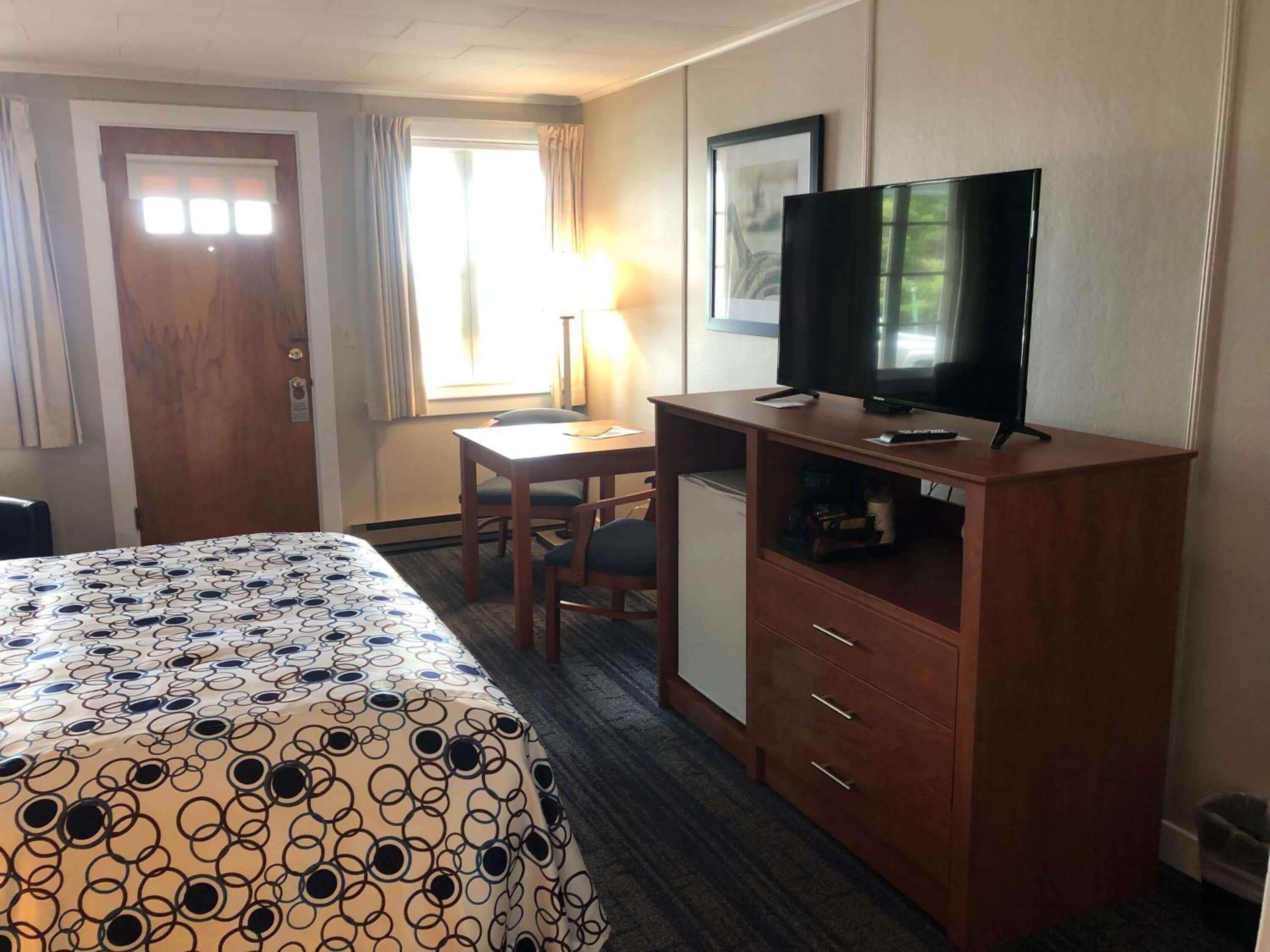 A hotel room with a bed, a desk, a television, and a small refrigerator.