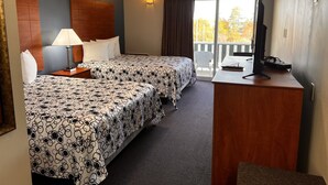 A hotel room with two beds, a desk with a TV, a lamp, and a view of the outdoors. - Edenbrook Motel (Bar Harbor)