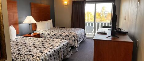 A hotel room with two beds, a desk with a TV, a lamp, and a view of the outdoors.