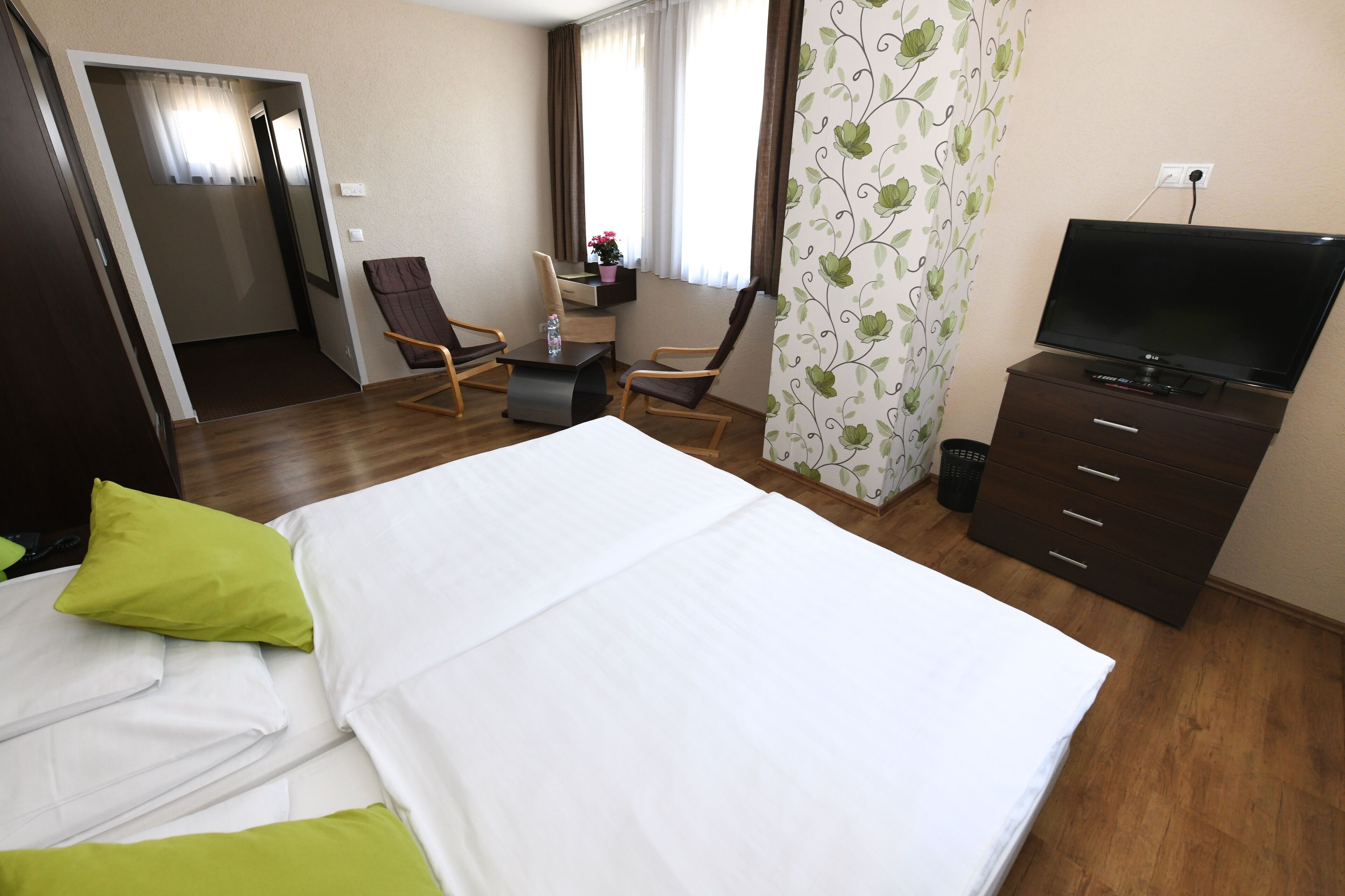 Een hotelkamer met een bed, twee stoelen, een bureau, een televisie en een raam met gordijnen.