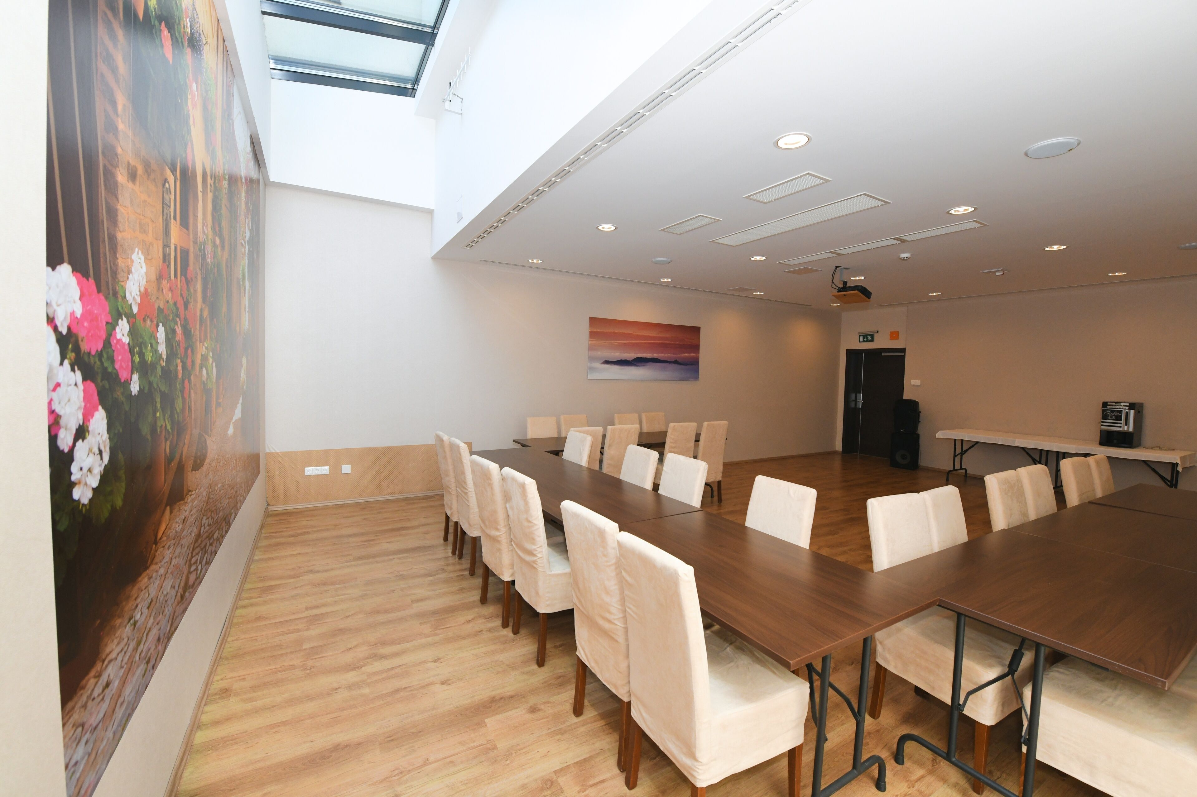 A conference room with a long table, white chairs, a painting on the wall, and a speaker on the right.
