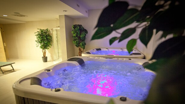 Zwei Whirlpools mit Wasserstrahlmassagen und LED-Beleuchtung, umgeben von Zimmerpflanzen und einer Sitzbank.