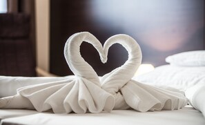 Un corazón hecho con toallas sobre una cama con sábanas blancas.