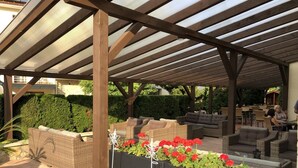 Ein Außenbereich mit Terrassenausstattung, Korbmöbeln, einer Pergola und Topfpflanzen.