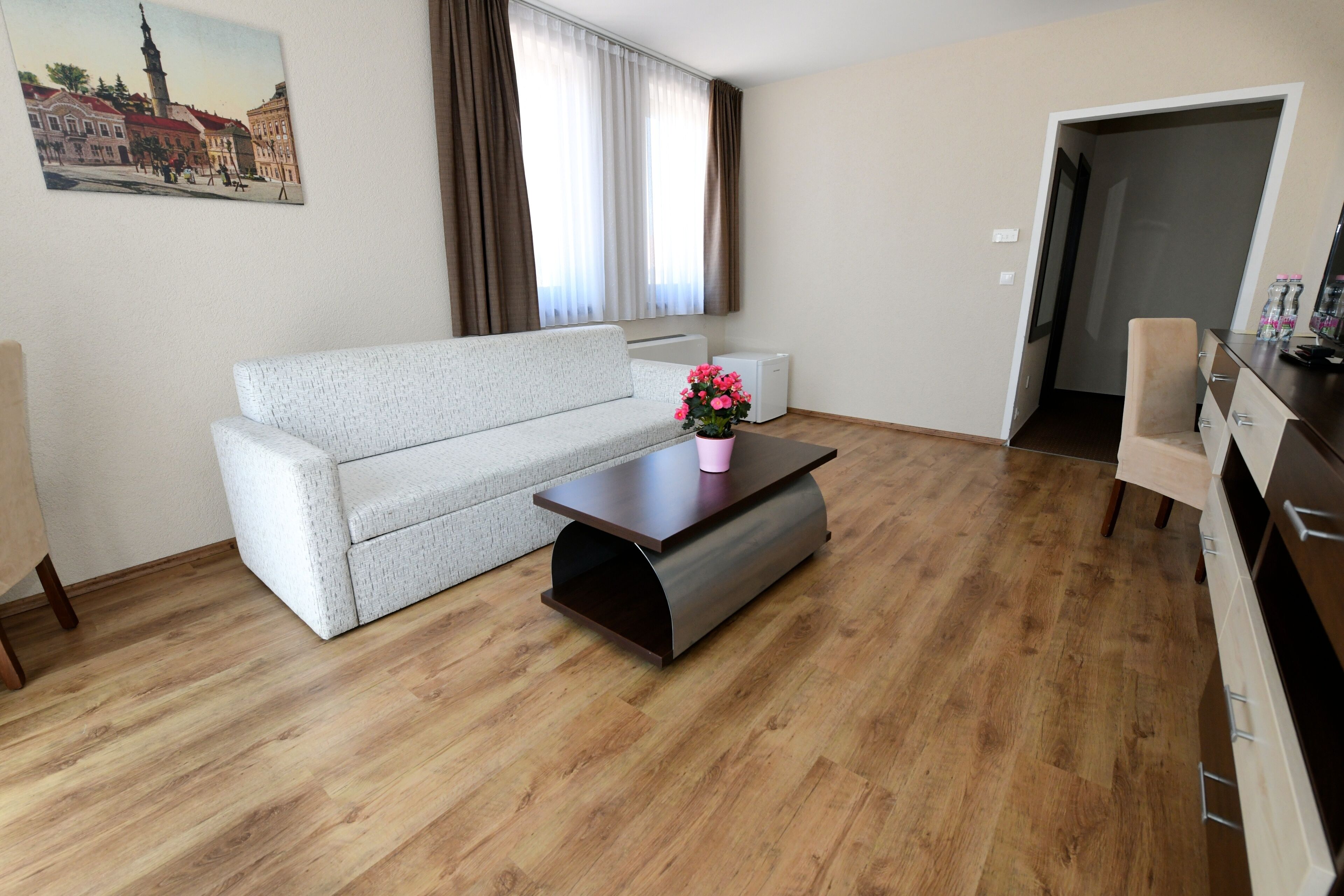 A living room with a sofa, a coffee table with a flower vase, a radiator, and a door leading to another room.