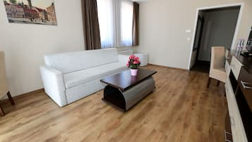 A living room with a sofa, a coffee table with a flower vase, a radiator, and a door leading to another room.