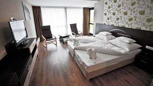 Ein Hotelzimmer mit einem großen Bett, zwei Sessel, einem Schreibtisch mit Fernseher und einem Fenster mit Vorhängen.