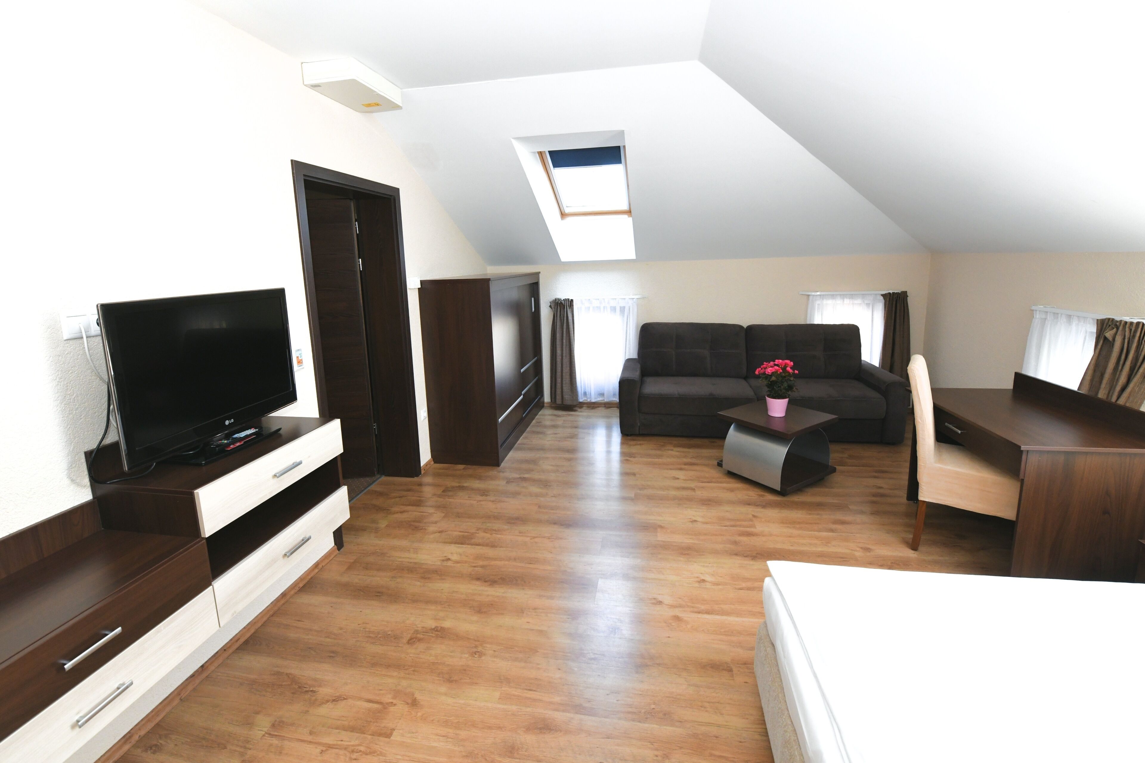 Un amplio loft con techo alto, tragaluz, un gran sofá oscuro, televisor de pantalla plana, escritorio de madera y zona de comedor.