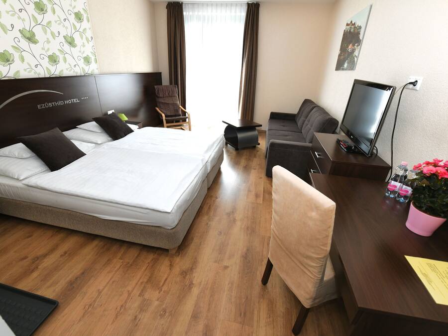 Habitación de hotel con cama, escritorio con computadora, silla, televisor y planta en maceta.