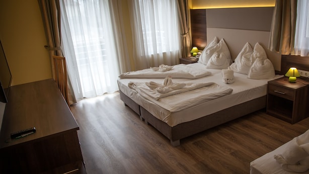 Habitación de hotel con cama, suelo de madera, una mesita de noche con lámpara y televisor sobre una mesa de madera.