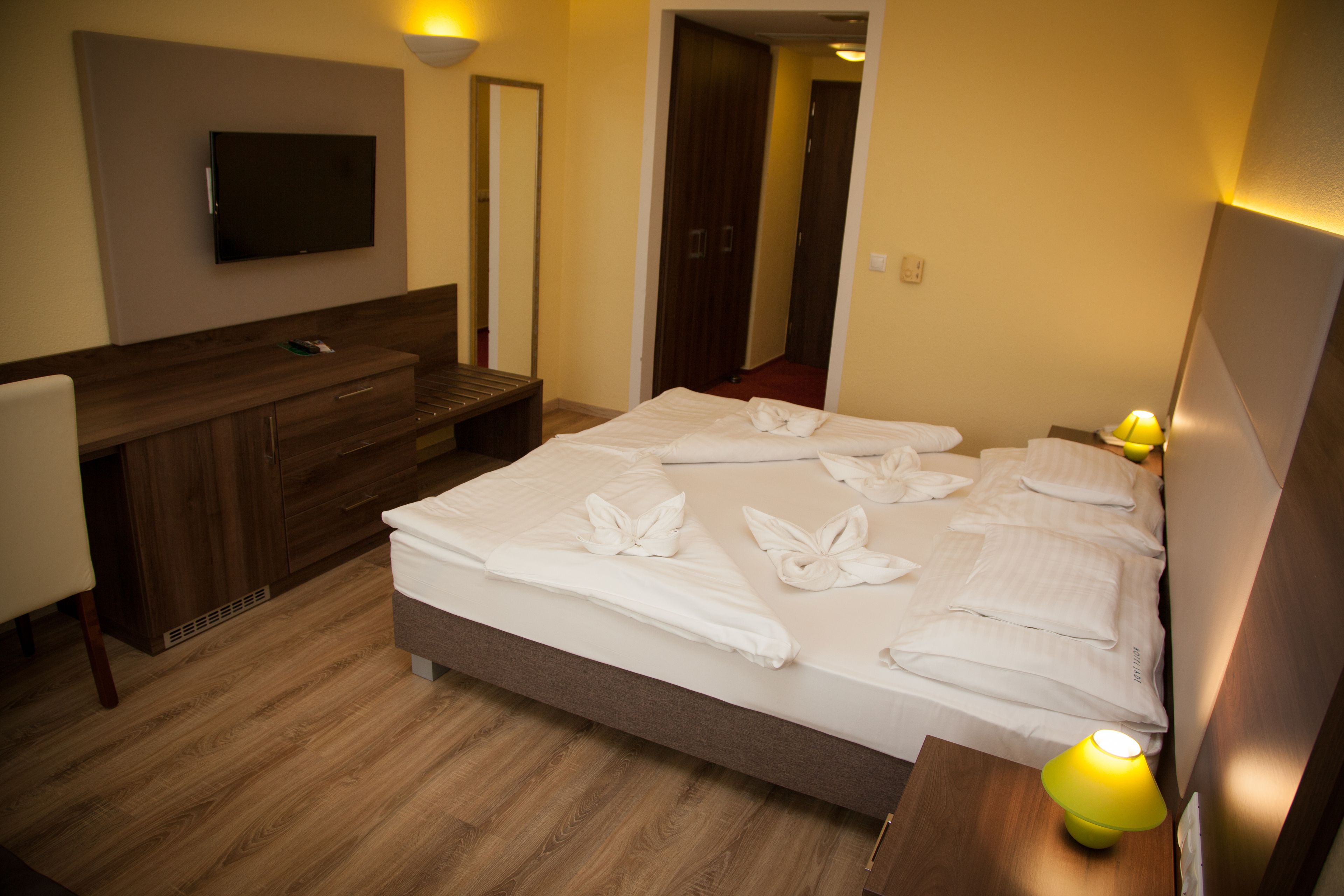 Una habitación de hotel con cama, mesita de noche, lámpara y televisor instalado en la pared.