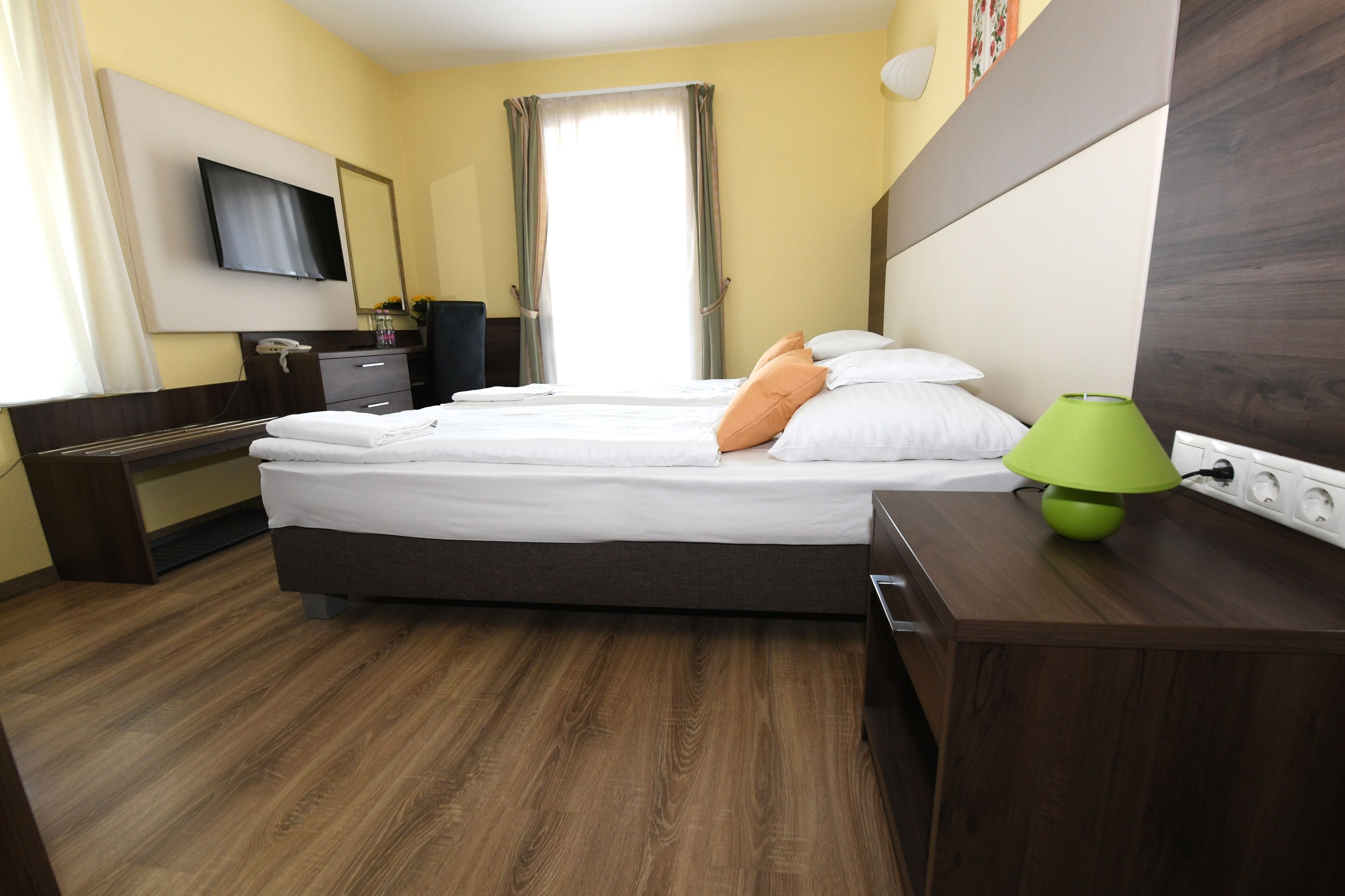 A hotel room with a bed, bedside table, lamp, and a TV mounted on the wall.