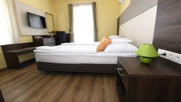A hotel room with a bed, bedside table, lamp, and a TV mounted on the wall.
